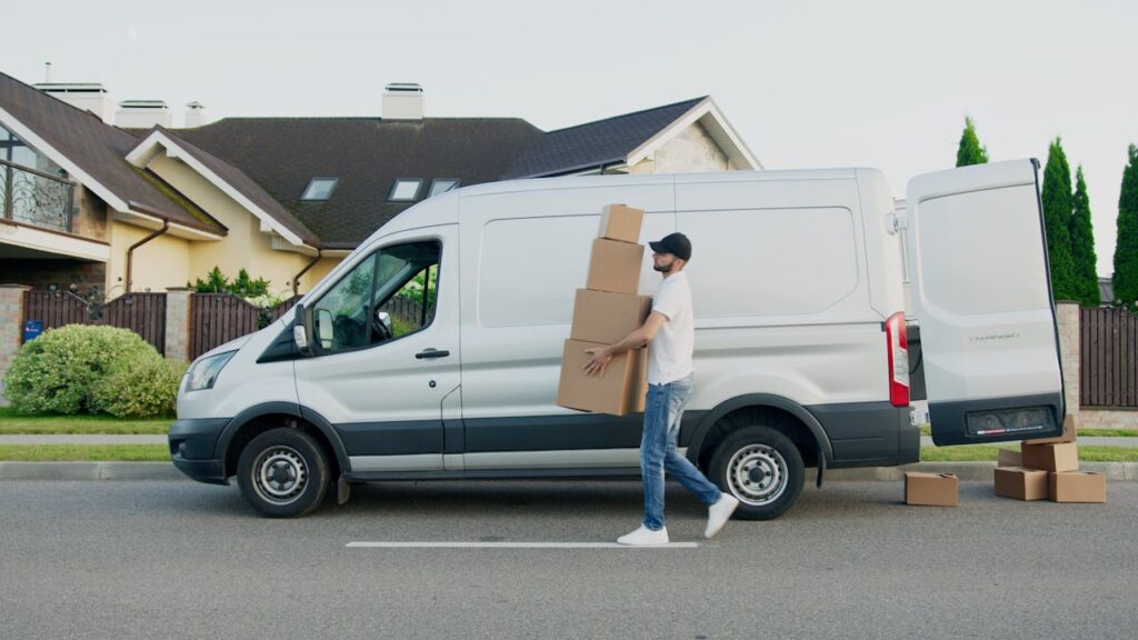 Everyone Is Tired, But No One Is Resting Properly Man unloading cardboard boxes from a delivery van in a suburban neighborhood street.