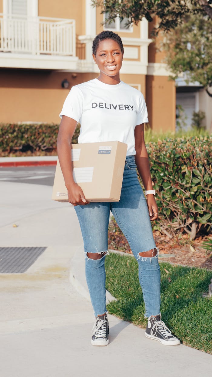 African American delivery woman smiling while holding a package outdoors during day.